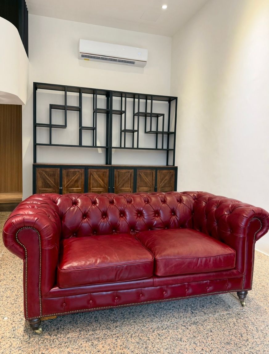 180公分寬的酒紅色 Chesterfield Style C 雙人全牛皮沙發，背靠訂製工業風鐵件木質層架，經典英倫手工拉扣工藝完美融入現代私宅設計。